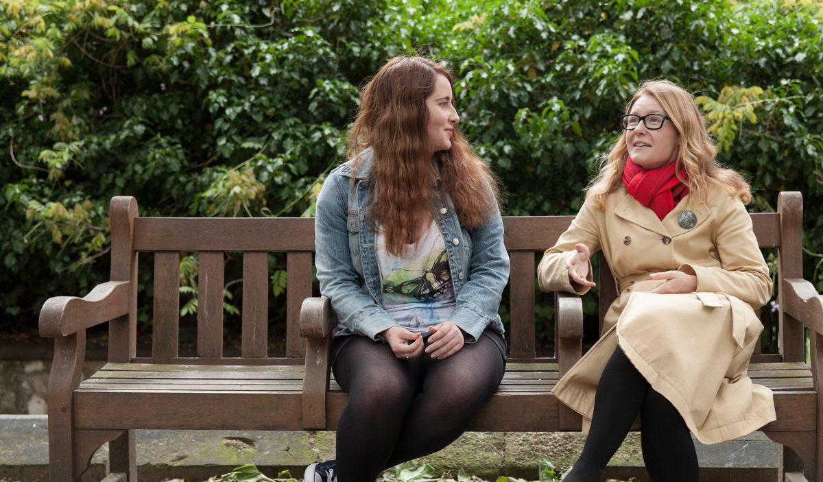 Two young women sat on a park bench, chatting to one another.