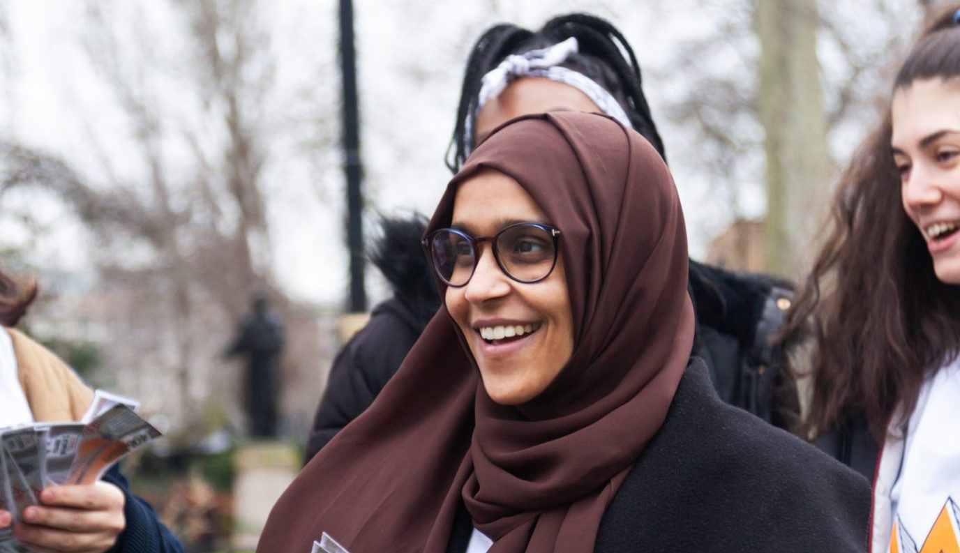 A young woman smiling, with two young women stood behind her outdoors.