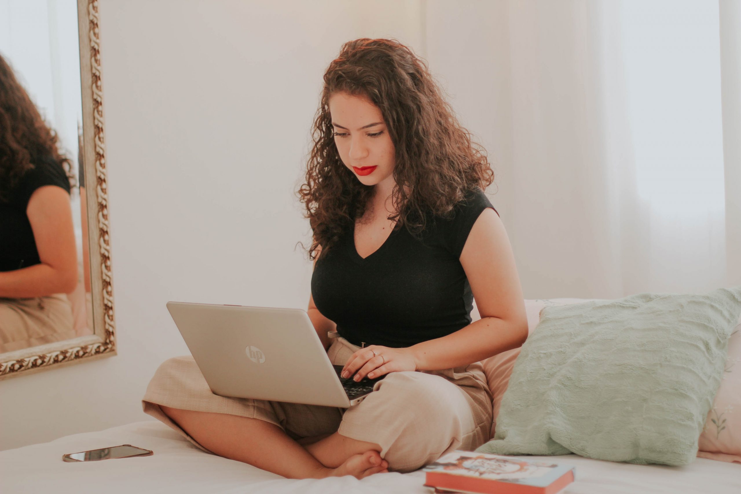 A young woman sat on her bed, typing on her laptop.