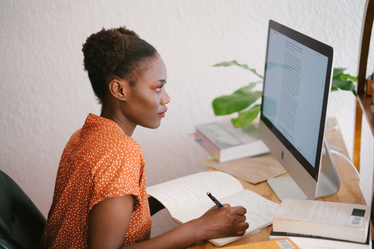 Young woman writing in a notebook looking at her computer