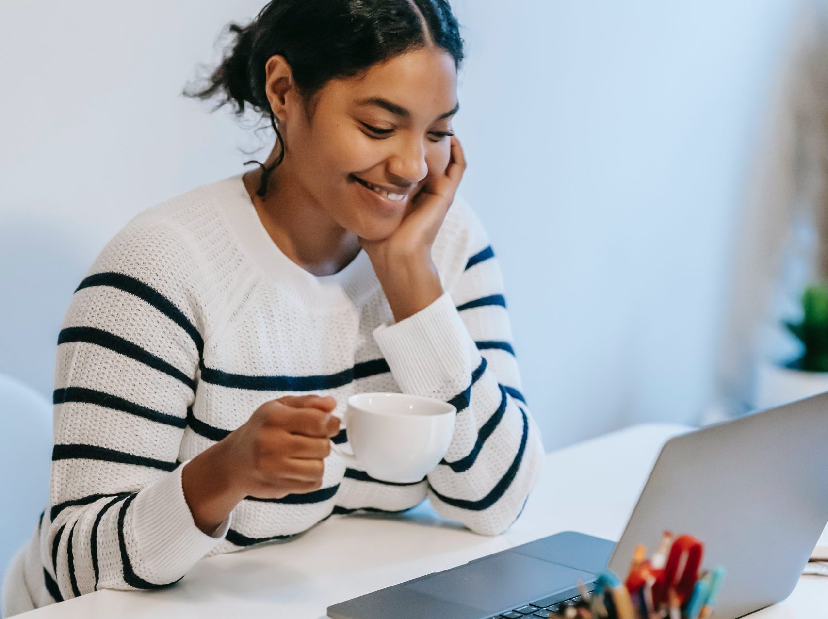 A young woman looking at her laptop holding a cup of tea