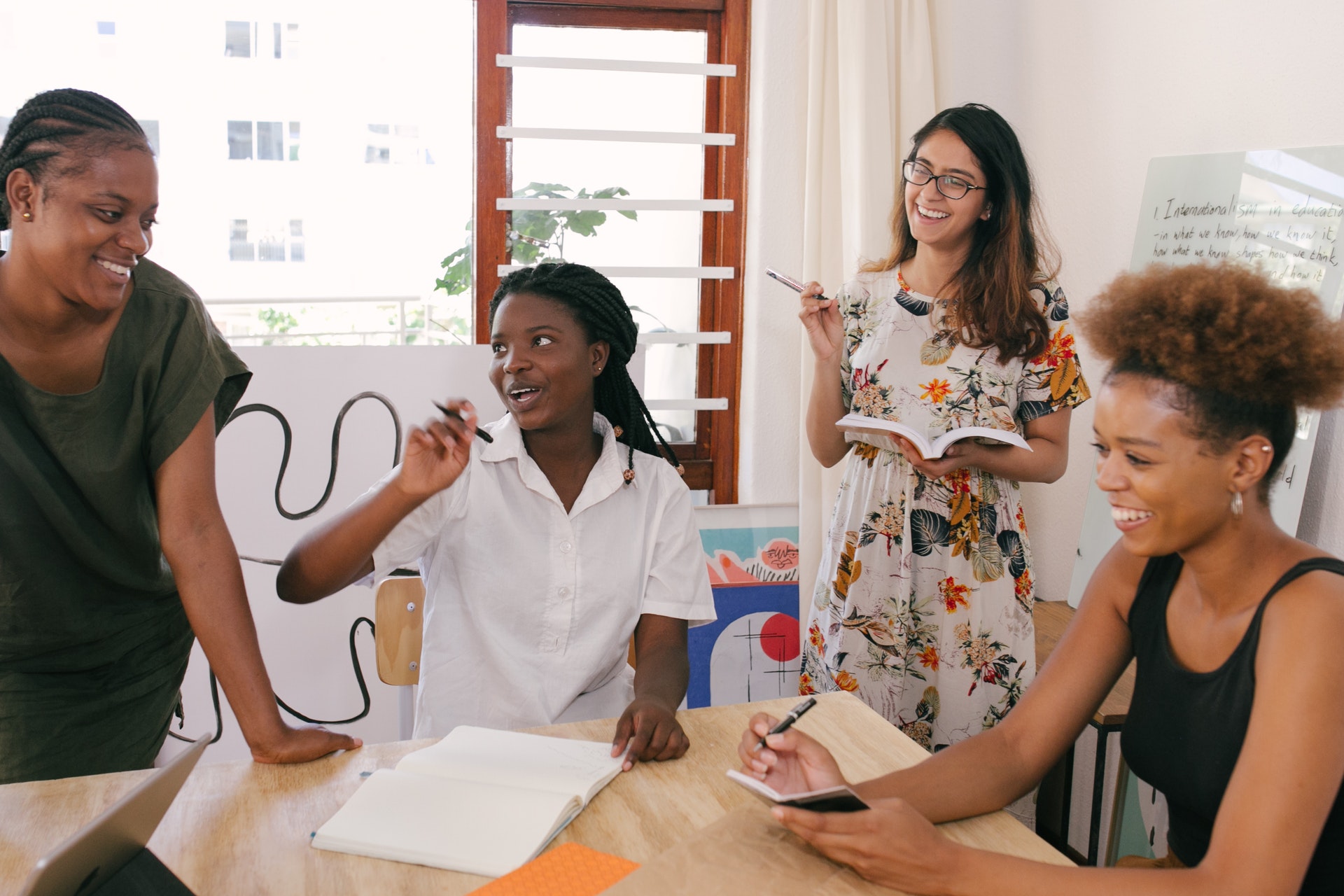 A group of young women holding notebooks talk around a table