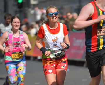 A woman wearing sunglasses and a Young Women's Trust vest is running and smiling