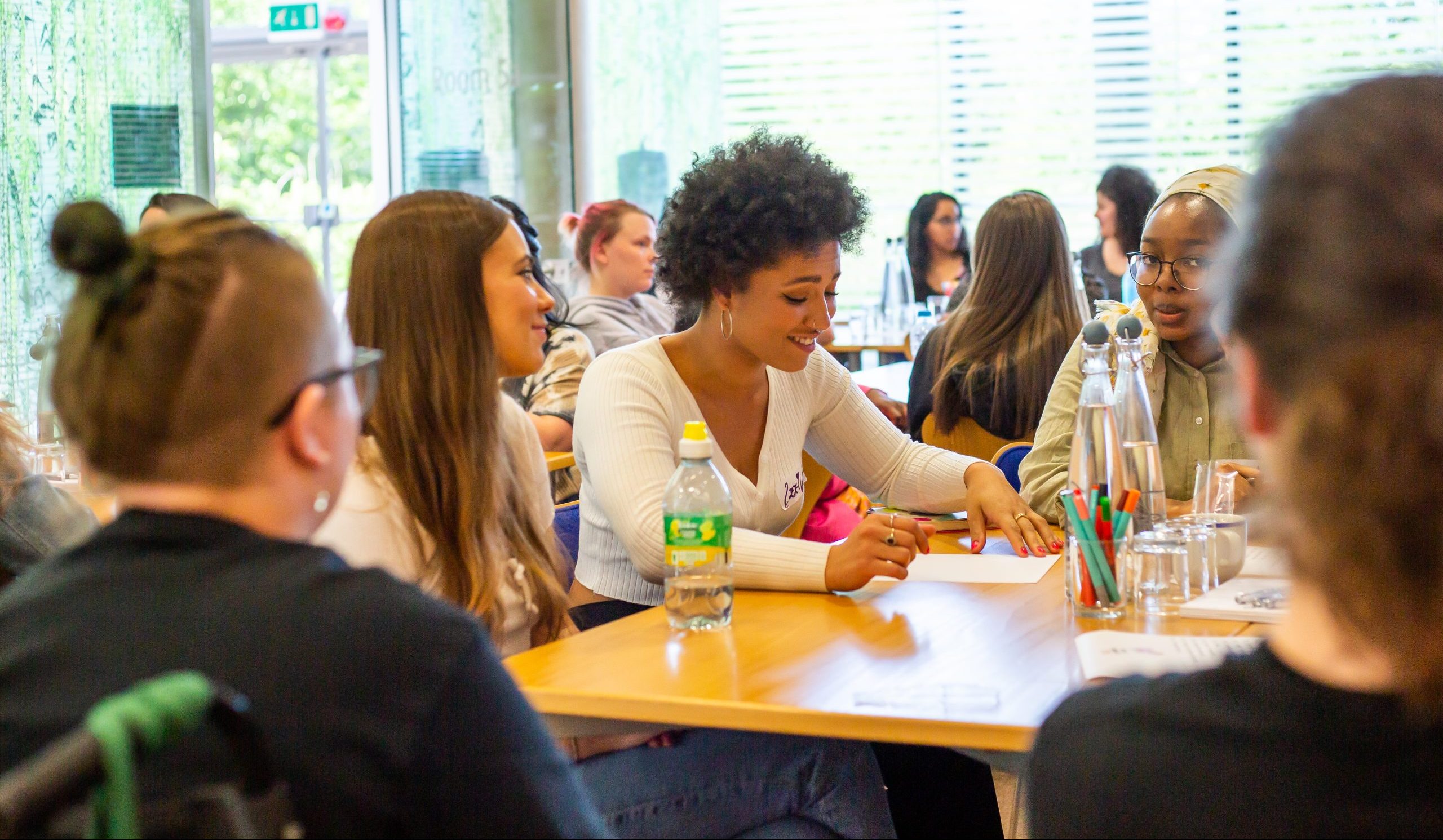 A group of young women in a workshop space, speaking to each other.