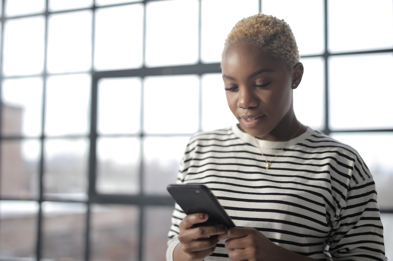 A woman with cropped hair looks at her phone with a hopeful expression