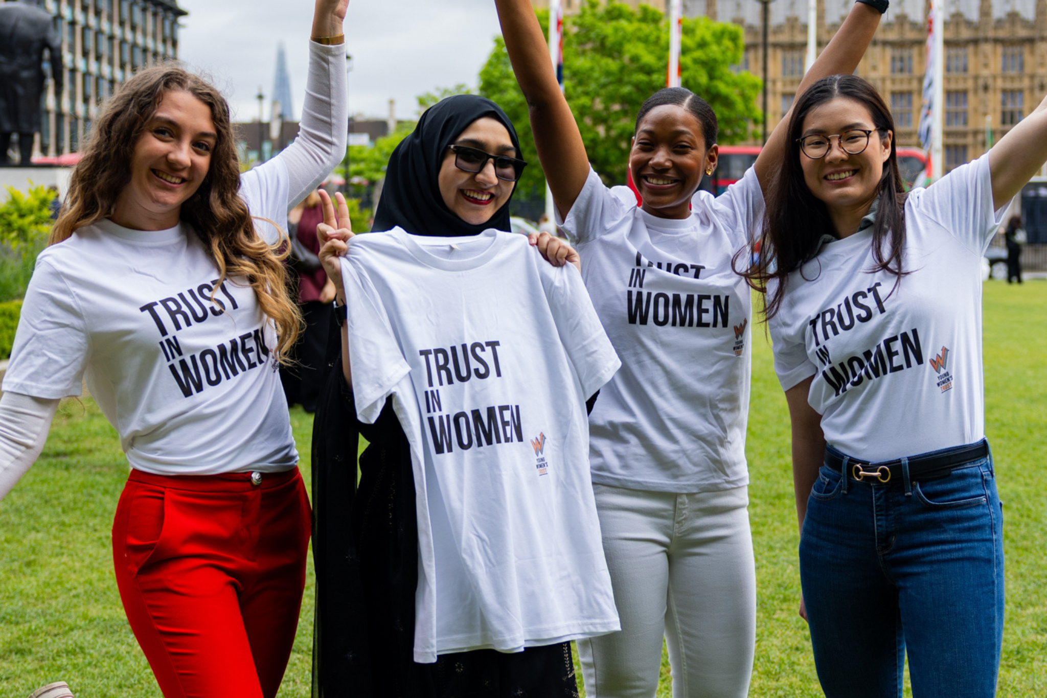 Four smiling young women outside the Houses of Parliament with tshirts that say 'trust in women'