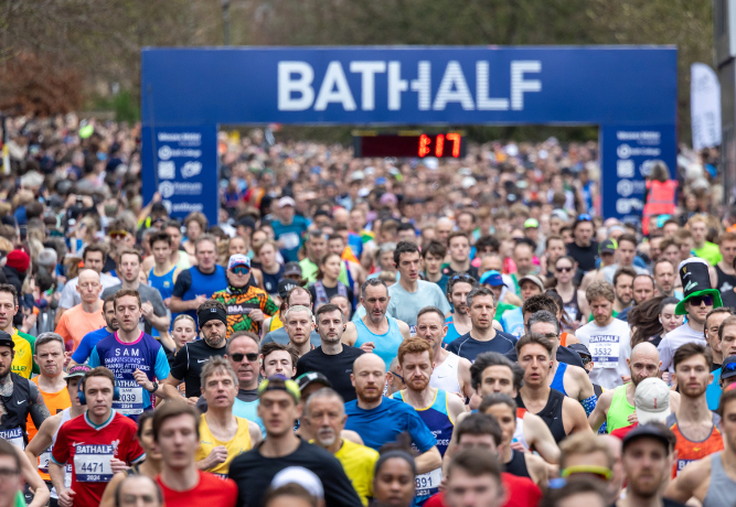 large crowd of runners passing under a banner with the Bath Half logo.