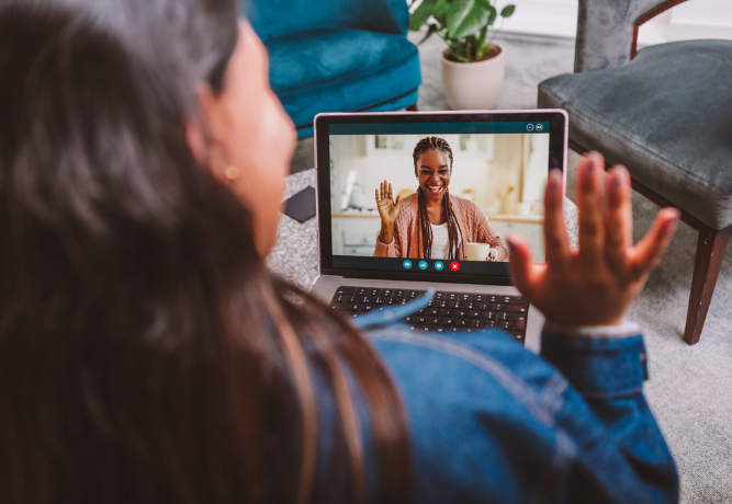 a woman having a video call with another woman, both smiling and waving at each other